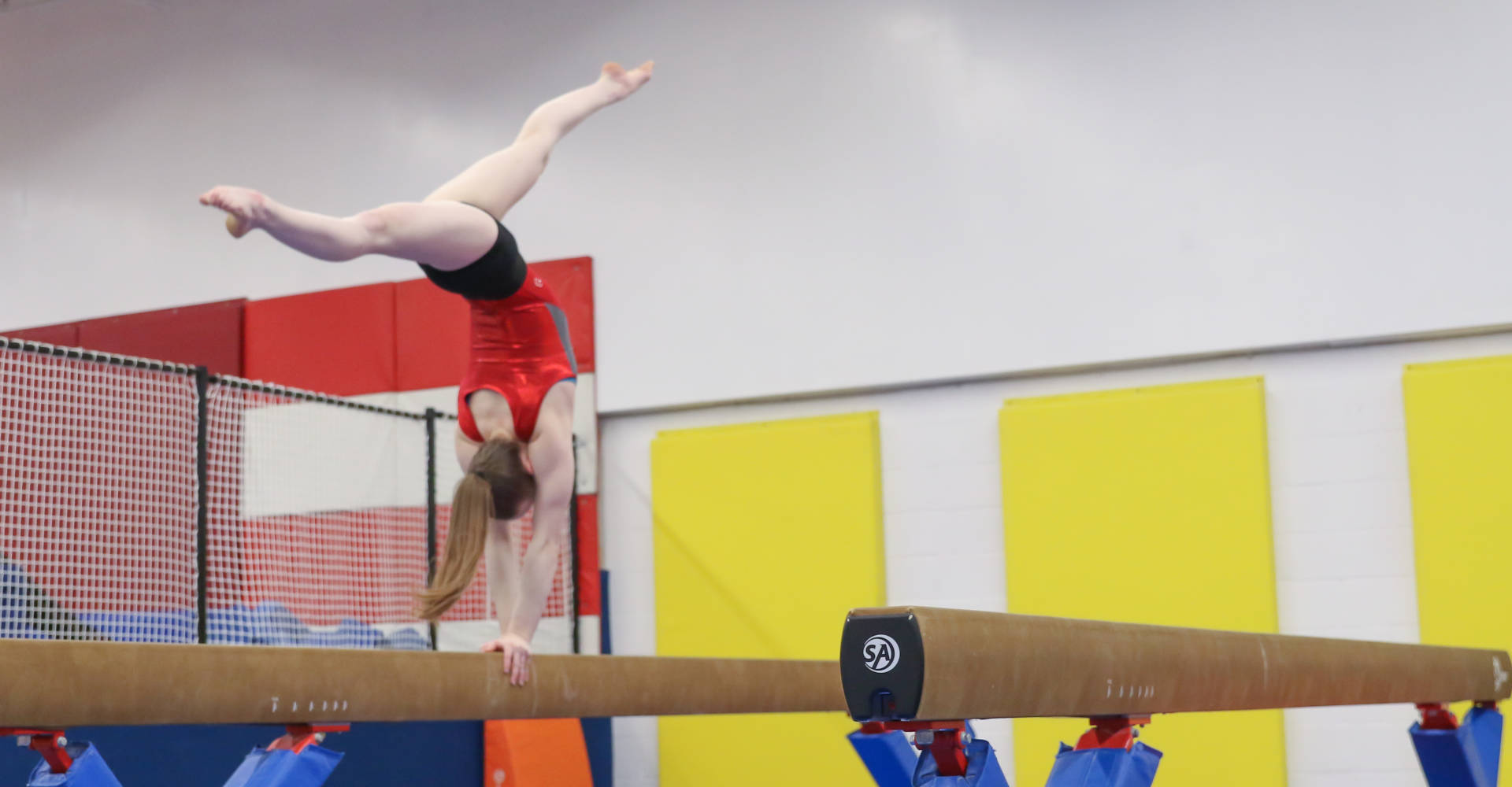 Gymnast performing a back walkover on a balance beam at Gymworld gymnastics facility in Northwest London