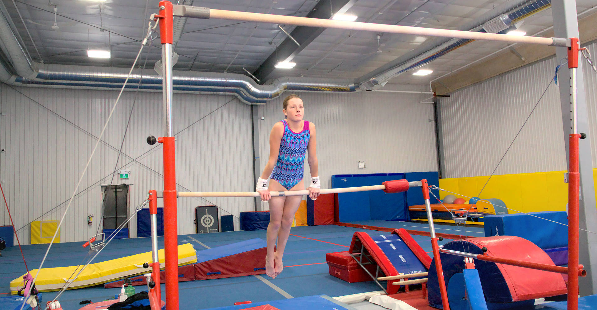 A young gymnast training on bars, holding front support, at the Gymworld Adventures in Gymnastics facility in London Ontario.