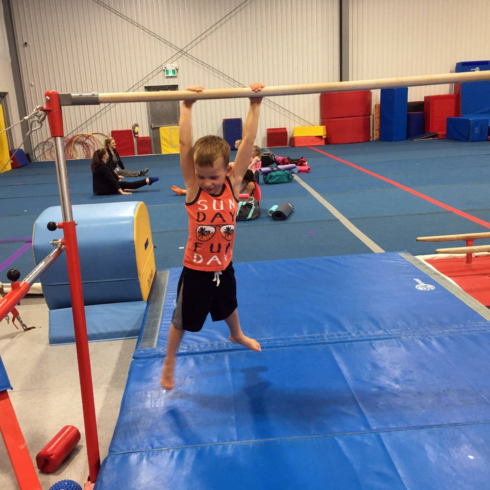 Coach looks on as young gymnast on a balance beam practices a back walkover at Gymworld Adventures in Gymnastics facility in North London.