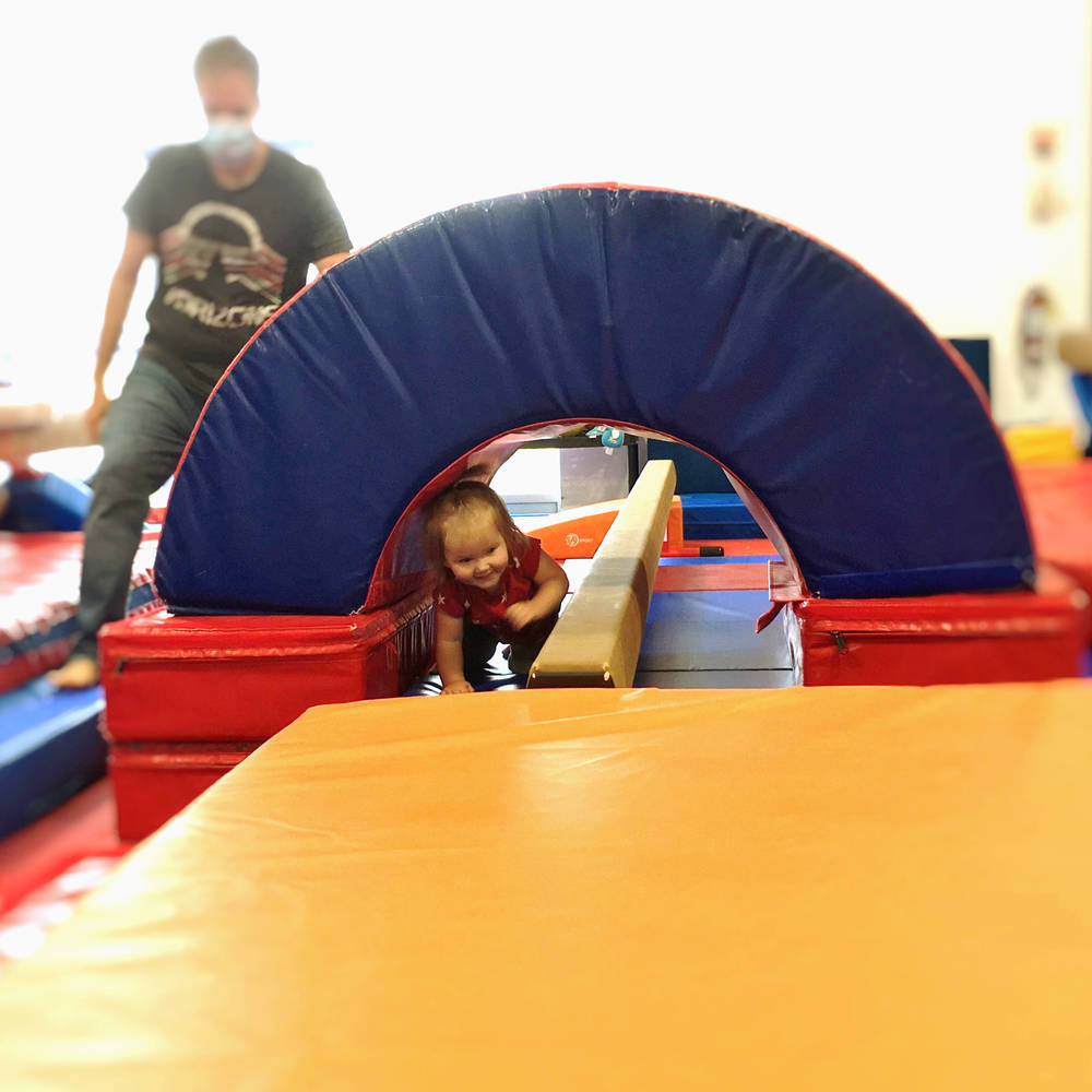 Coach looks on as young gymnast on a balance beam practices a back walkover at Gymworld Adventures in Gymnastics facility in North London.